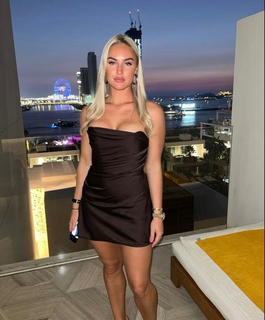 Golfer Charley Hull posing in a strapless dress on a balcony overlooking a city skyline at dusk.