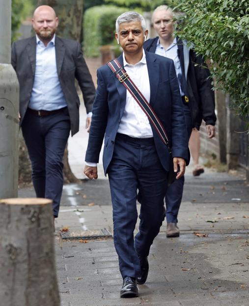 Sadiq Khan walking on a sidewalk with two security guards behind him.