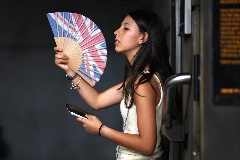 A woman uses a fan with a British flag design to cool down.