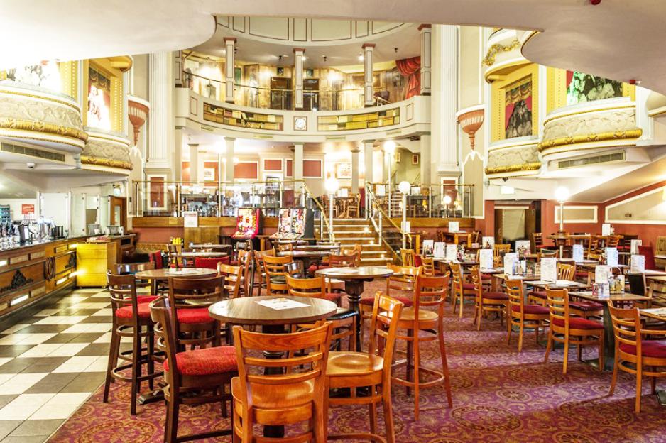 Interior of JD Wetherspoons in Llandudno, showing tables and chairs set up in a large hall with a balcony and bar.