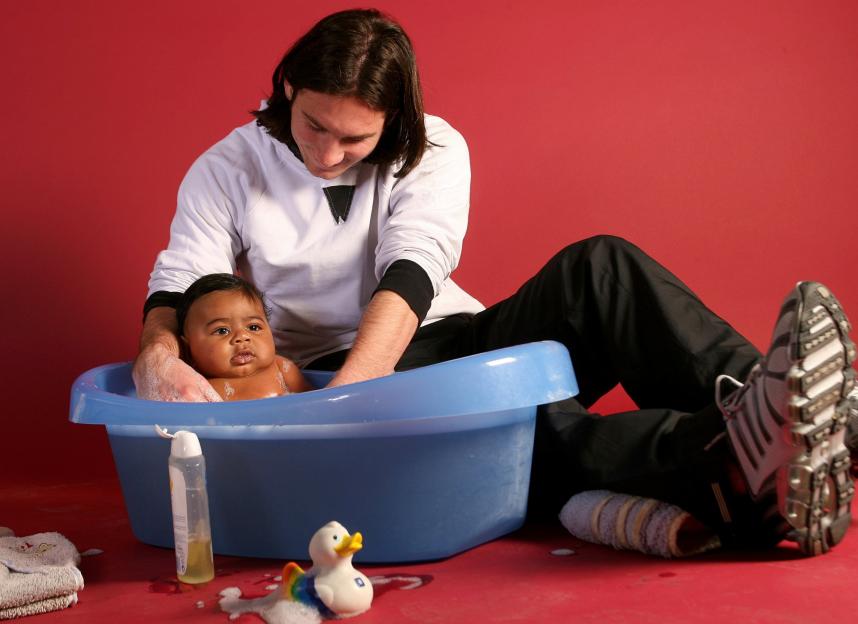 A man bathing a baby in a blue tub with a red background.