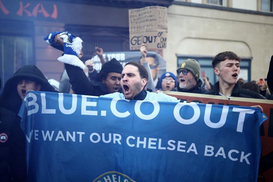 Chelsea fans protesting with banners saying "BLUE.CO OUT" and "WE WANT OUR CHELSEA BACK".