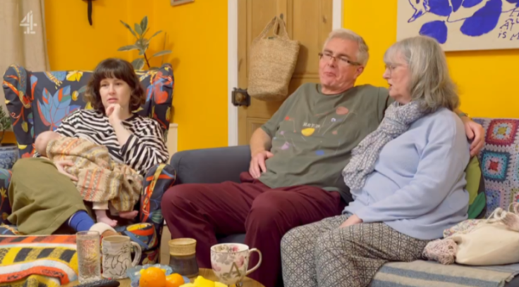 Three people on couches in a brightly colored living room, one holding a baby.