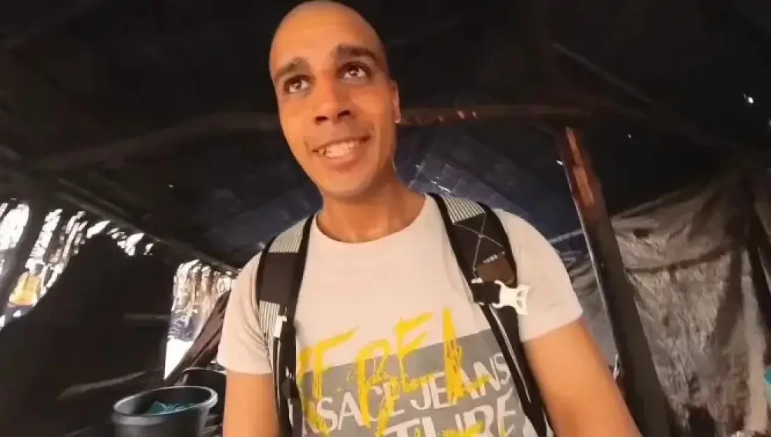 Man with a shaved head and backpack smiling.