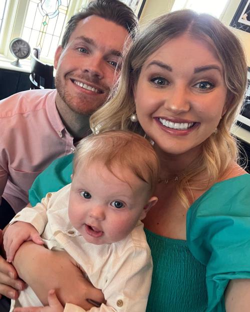 Amy Hart, her partner, and their baby Stanley smiling at the camera.