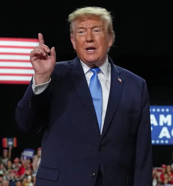 President Donald Trump points his index finger upward while speaking at a campaign rally before a crowd.