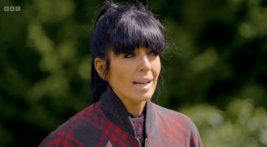 Claudia Winkleman wearing a red and grey plaid jacket outdoors.