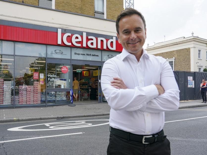 Richard Walker, Managing Director of Iceland Foods, stands smiling with arms crossed in front of an Iceland supermarket.