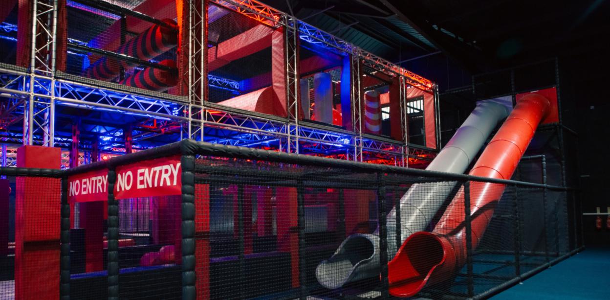Indoor adventure park with red and grey slides and a multi-level climbing structure.