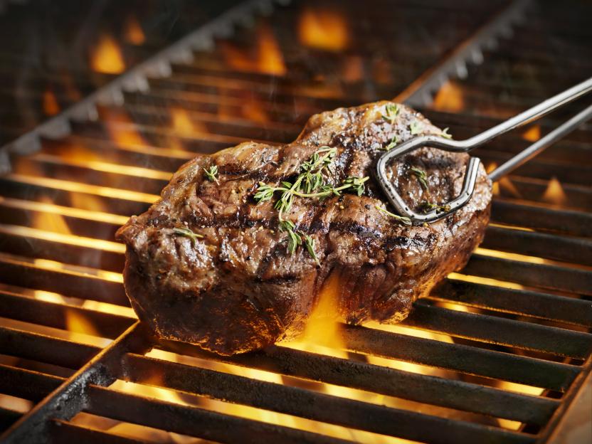 Juicy sirloin steak with fresh thyme being grilled over flames.