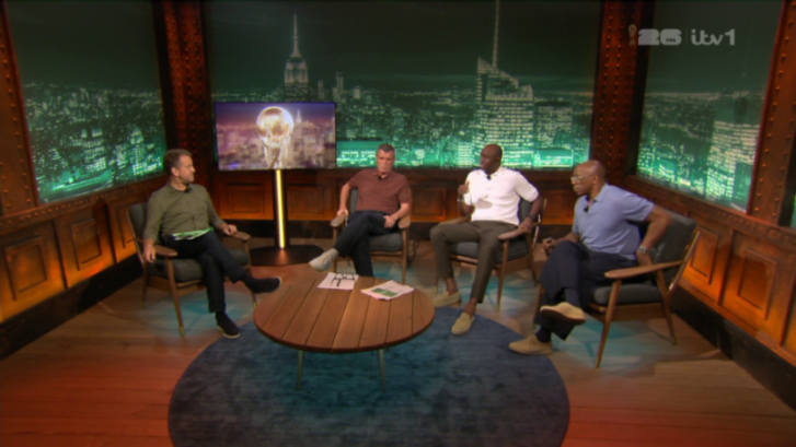 Four men sitting in a studio with a city skyline backdrop, discussing the World Cup trophy shown on a screen.