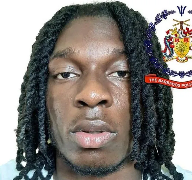 Headshot of a Black man with dreadlocks and a light beard, with the Barbados Police crest in the top right corner.