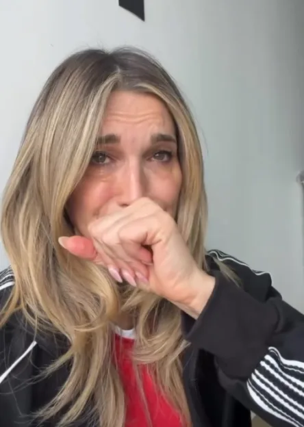 A blonde woman crying, holding her hand over her mouth.