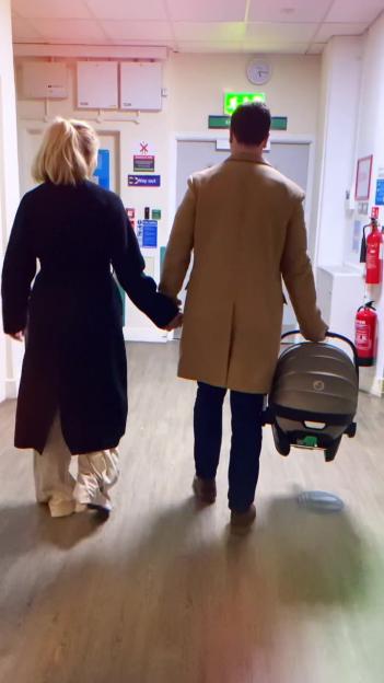 Richard Fleeshman and his partner leaving the hospital with their newborn in a carrier.