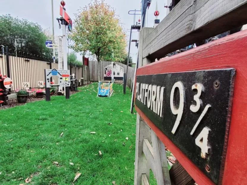 A sign reading "Platform 9 3/4" in the foreground, with a garden area and model railway elements in the background.