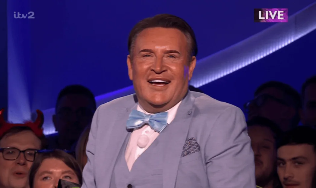 Gregg Wallace smiling in a light blue suit and bow tie in the audience on ITV2.