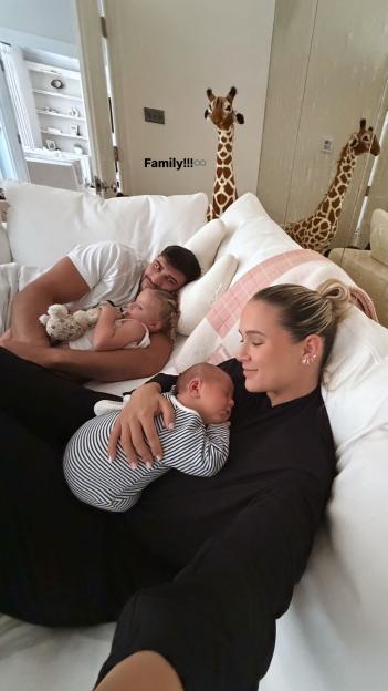 Molly-Mae Hague holding her baby Midas, with Tommy Fury and their daughter Bambi resting on the couch.