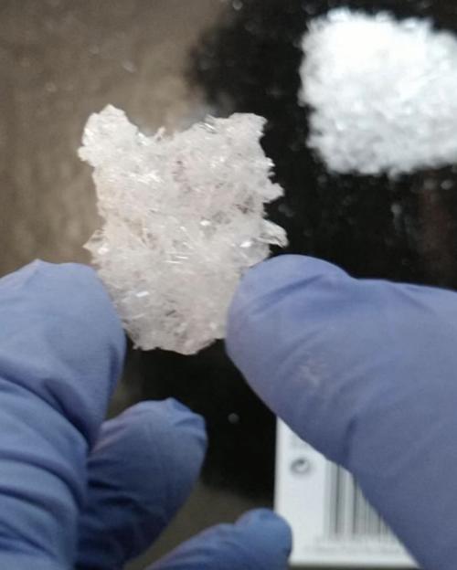 A close-up of two blue-gloved hands holding a large chunk of white crystalline drug.