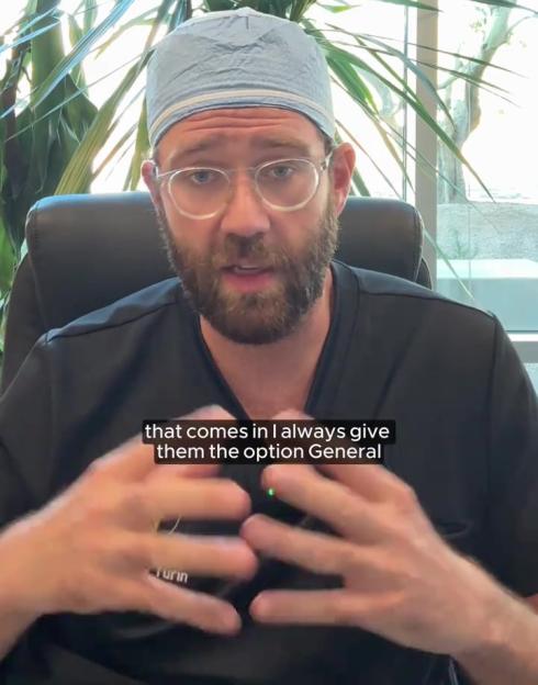 A bearded man wearing a surgical cap and glasses gestures with his hands while speaking.