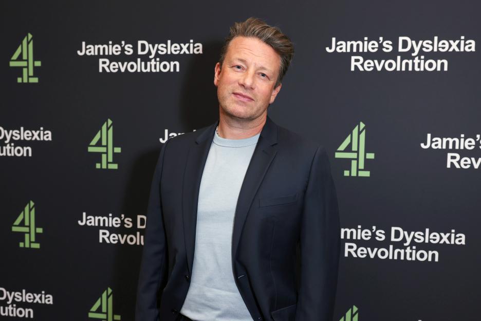 Jamie Oliver standing in front of a black backdrop with a green "4" logo and "Jamie's Dyslexia Revolution" text.