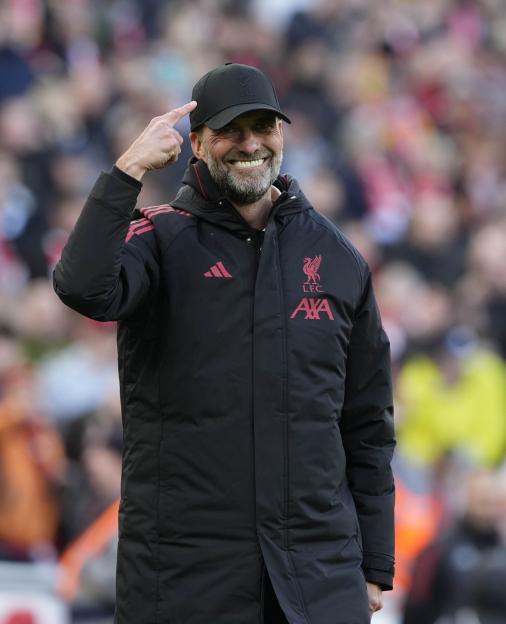 Jürgen Klopp smiling and pointing to his black LFC cap at Anfield.