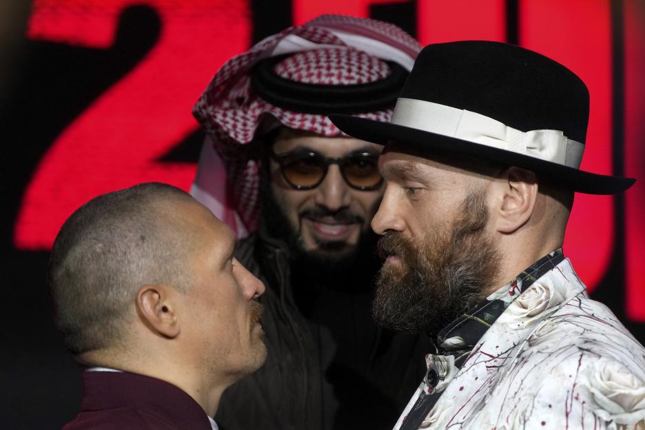 Boxers Oleksandr Usyk and Tyson Fury face off with Turki Al-Sheik between them at a press conference.