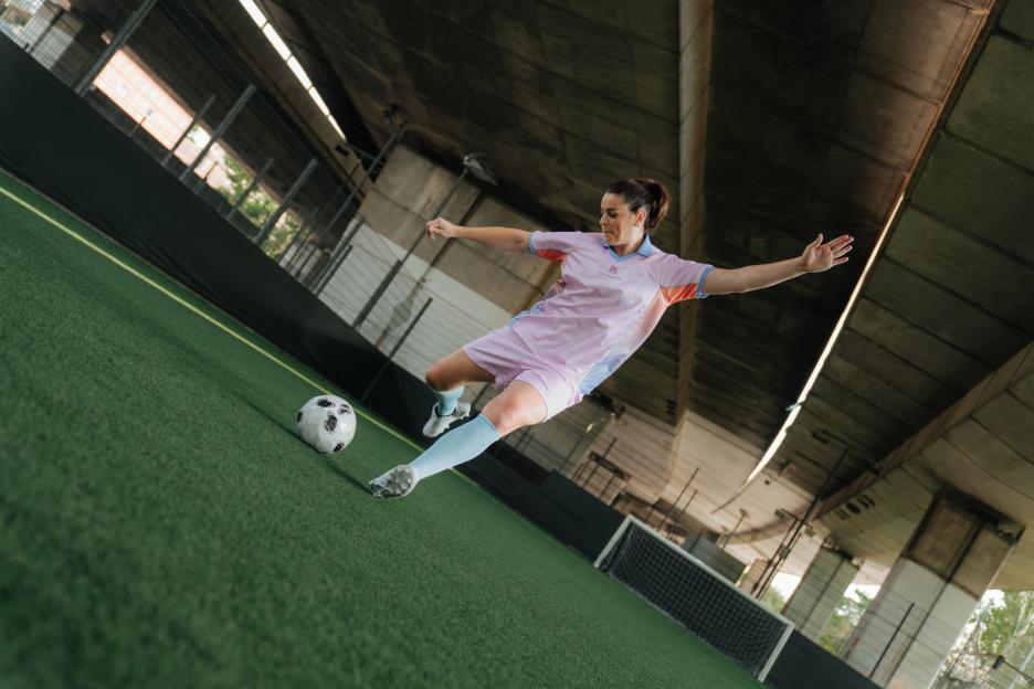 Jen Beattie kicking a soccer ball on a green turf field, wearing a pink and blue uniform.