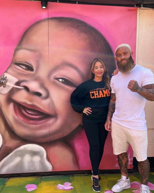 Ashley Cain and Safiyya Vorajee standing in front of a mural of their daughter Azaylia.