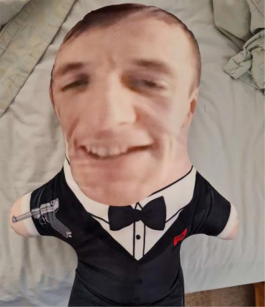 A pillow of Dylan Westall's face on a tuxedo-wearing body, with a pistol design on the left arm.