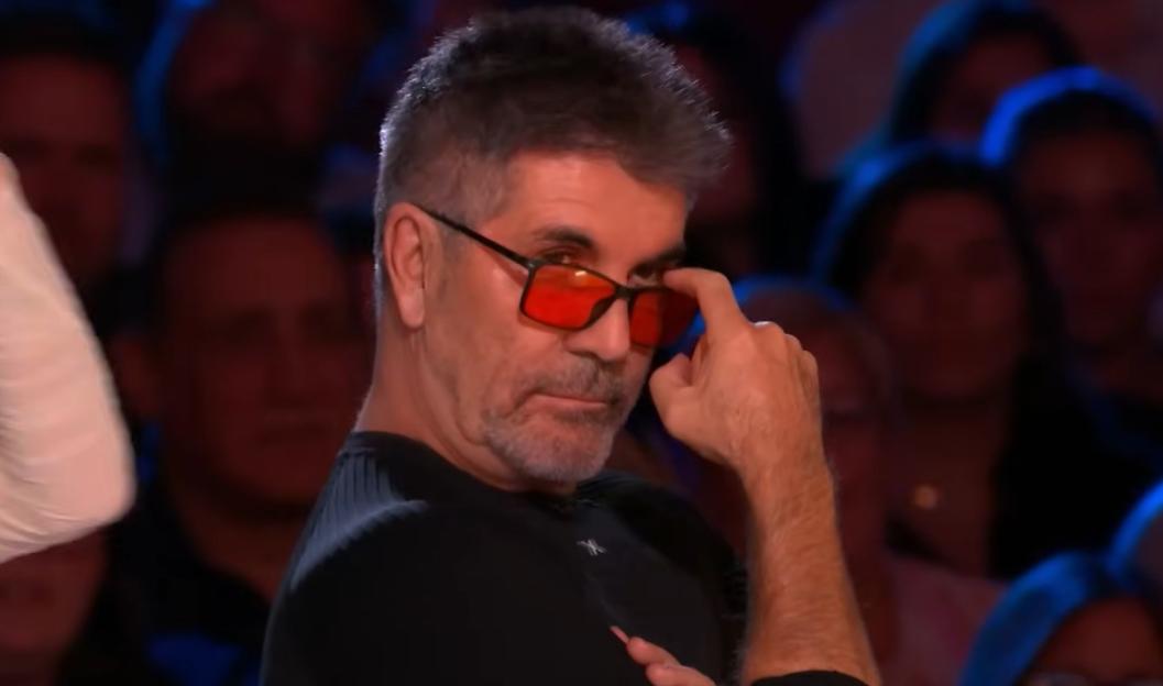 Simon Cowell wearing red-tinted glasses, looking directly at the camera.