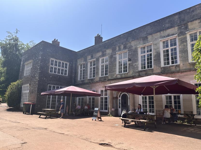Outdoor patio seating with picnic tables and red umbrellas in front of a stone building.