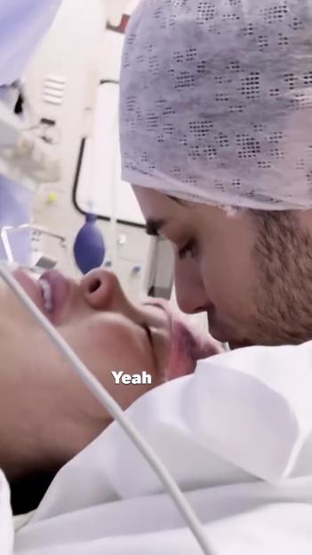 Marnie Simpson, in a hospital bed, looking up at a man in a surgical cap with equipment in the background.