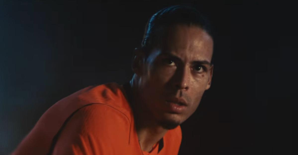 Virgil Van Dijk looking intensely forward, lit by an orange glow against a dark background.