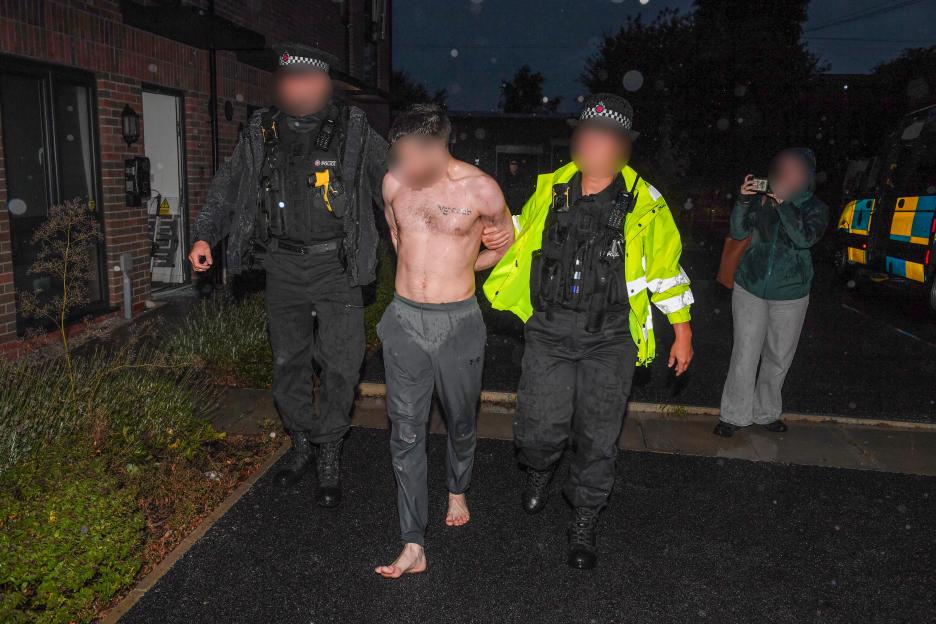 Police escorting an arrested, shirtless, handcuffed man who escaped from a window.