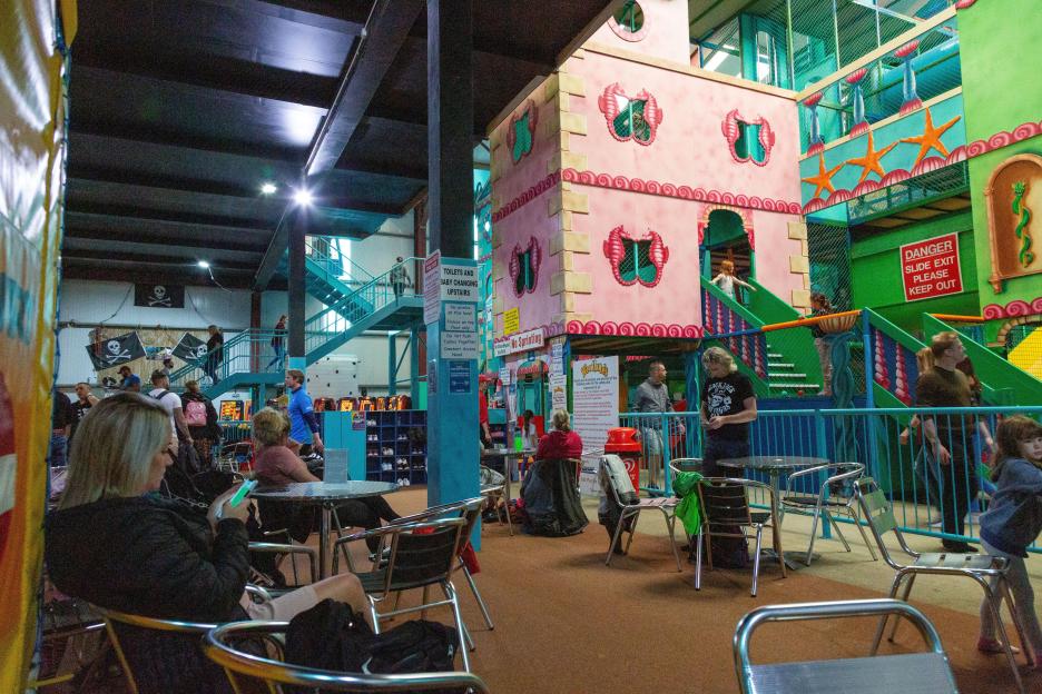 Sea Dragon indoor adventure soft play area with families, pirate flags, and a pink building with seahorse decorations.