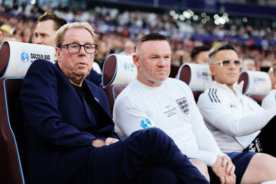 Harry Redknapp, Wayne Rooney, and Robbie Williams sitting in the Soccer Aid for UNICEF 2026 dugout at London Stadium.