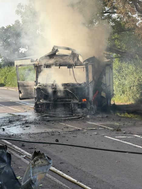 A burnt-out fire engine on a road with smoke still rising from it.
