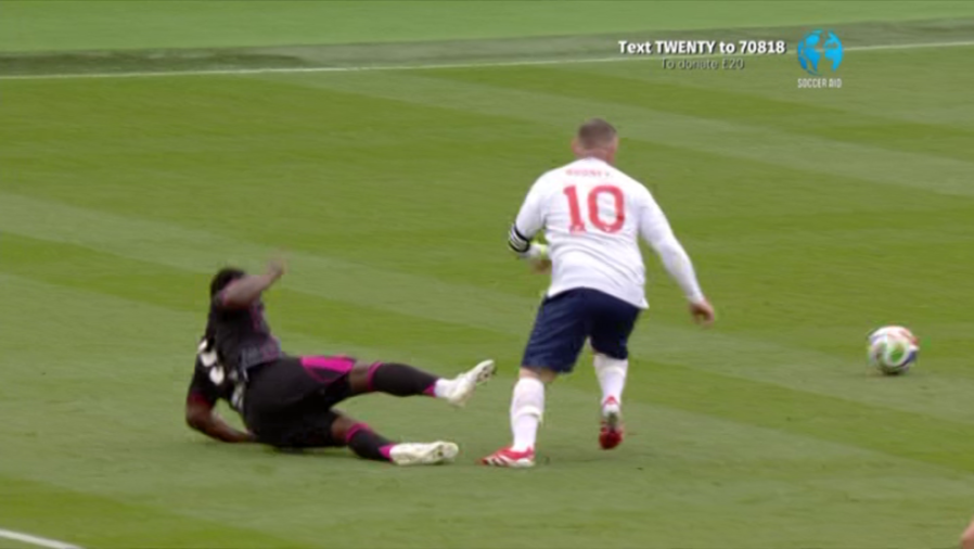 A soccer player wearing a white jersey with the number 10 runs past another player who has fallen to the ground.