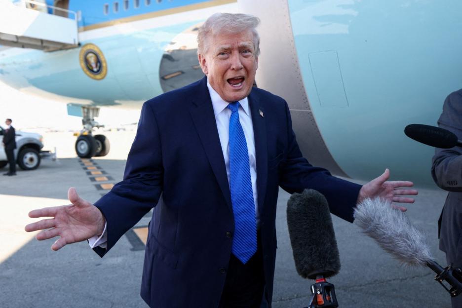 U.S. President Donald Trump speaking to microphones with a plane in the background.