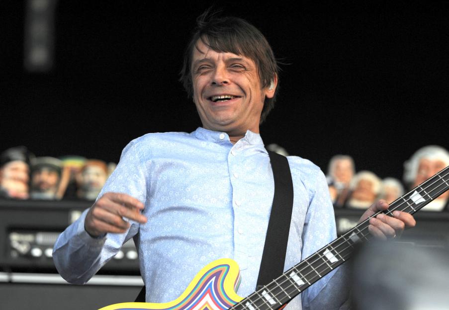 Mani of The Stone Roses playing bass guitar and laughing on stage.