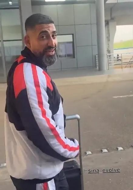 Sina Ghami looking over his shoulder at the camera while pulling a suitcase.