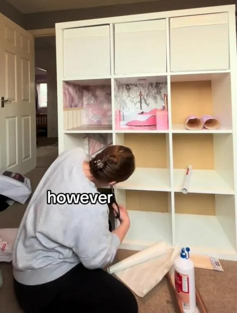 A person cutting decorative paper to make a Barbie dollhouse from an IKEA Kallax unit.