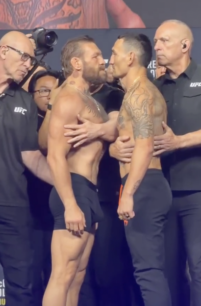 Two UFC fighters face off intensely at a weigh-in, separated by officials.