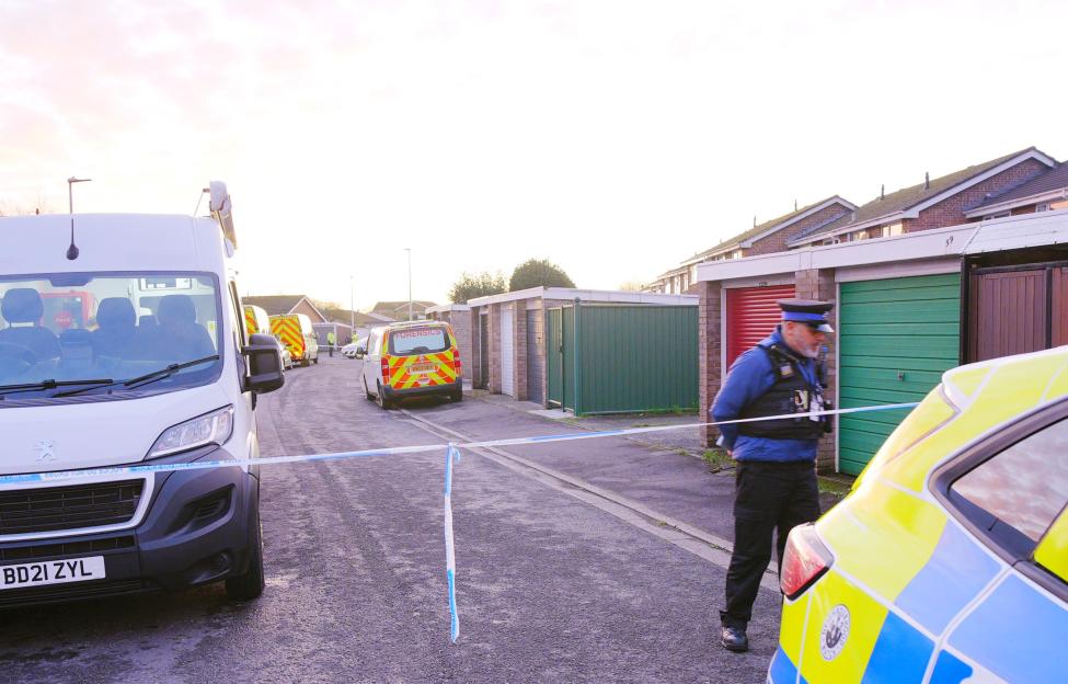 Police officers and forensics vans at a crime scene in a residential area, marked off with blue and white tape.