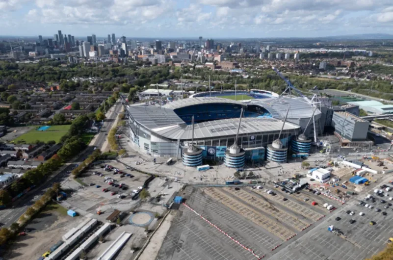Aerial view of Etihad Stadium in Manchester, with the city skyline in the background.