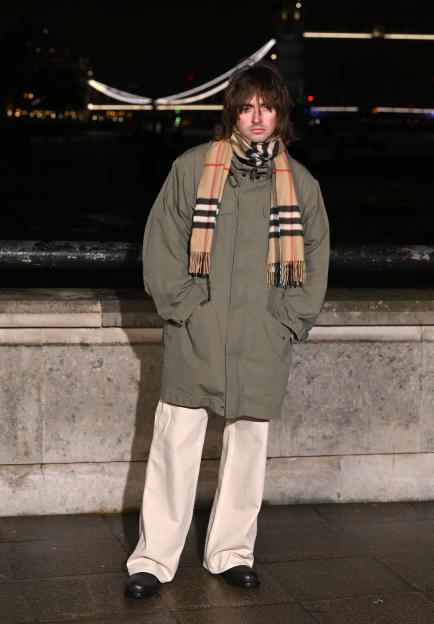 Gene Gallagher wearing a Burberry scarf and an olive green coat, standing outdoors at night.