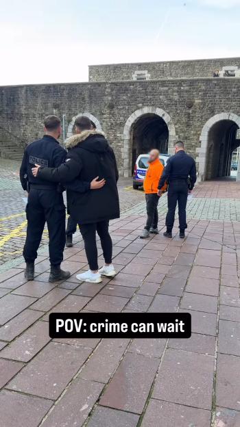 A man in a black coat and a police officer with their arms around each other next to a man in an orange jacket with handcuffs and another police officer.