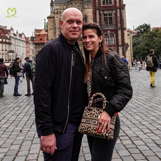 A bald man and a woman with long brown hair standing on a cobblestone street.