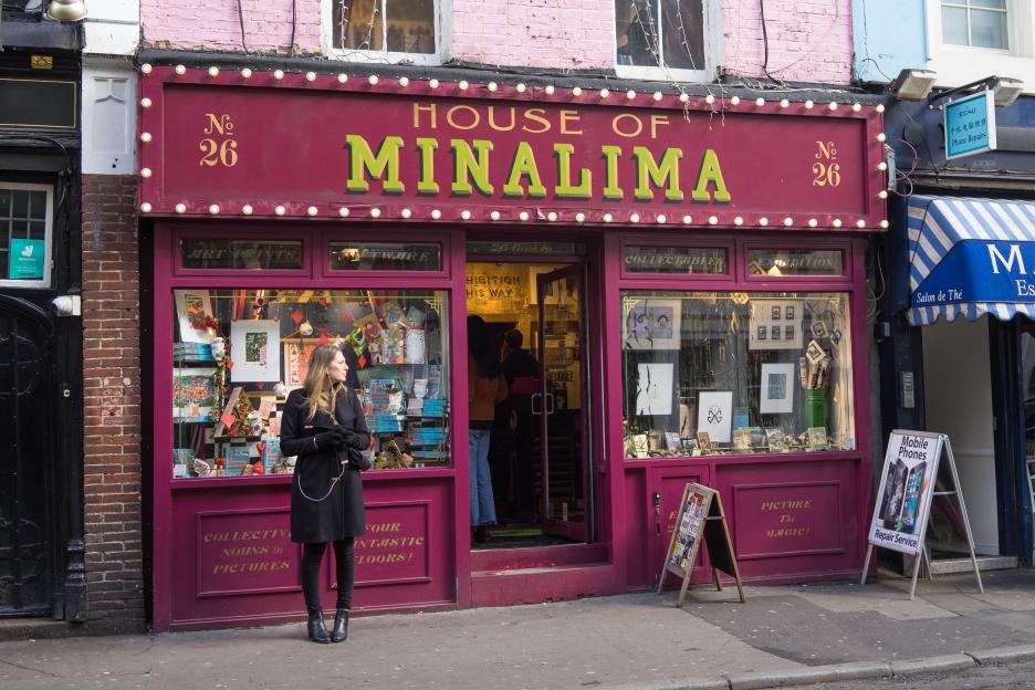 A woman in a black coat stands in front of the House of Minalima wizard magic shop in the style of Harry Potter in London.