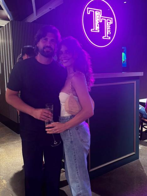 Dan Edgar and Chloe Lewis posing for a photo under a neon light sign.